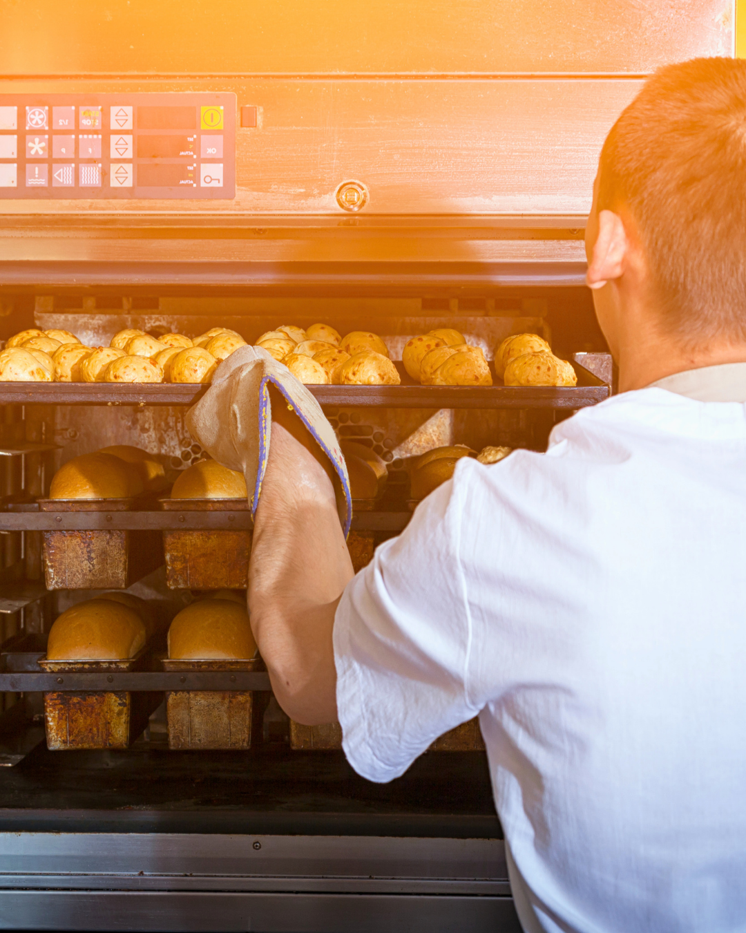 Baker placing trays of freshly baked bread into a commercial oven.