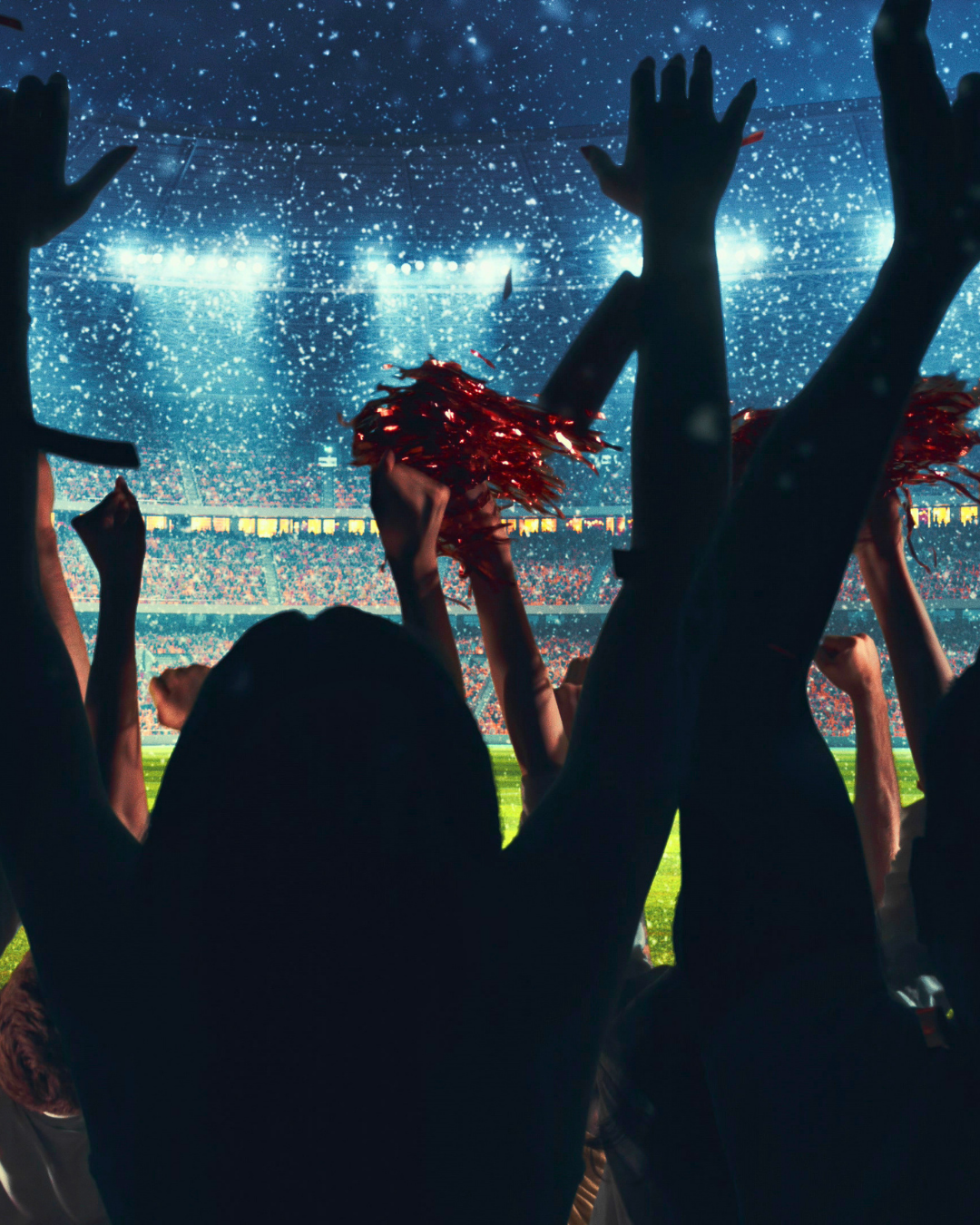 Football fans raising their hands and cheering inside a packed stadium during a match.